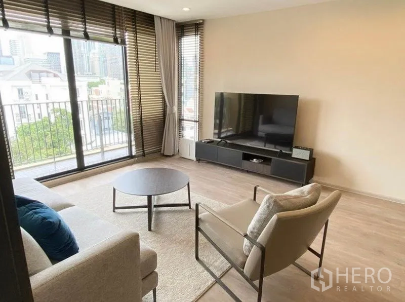 Condominium for rent in Pathum Wan, Bangkok - Bright lounge with TV console, city-view balcony, and large sliding glass doors with blinds.