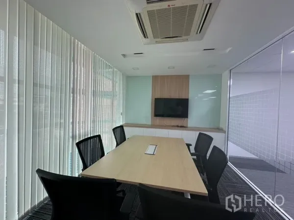 Office Space for rent - Small meeting room with six chairs, a long table, TV screen and vertical blinds.