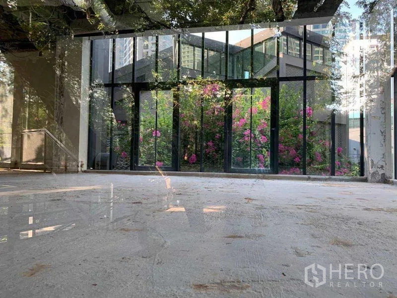 办公空间 出租在Khlong Toei, Bangkok - 采光充足的空置办公区，落地玻璃面向粉色花丛与绿植花园。