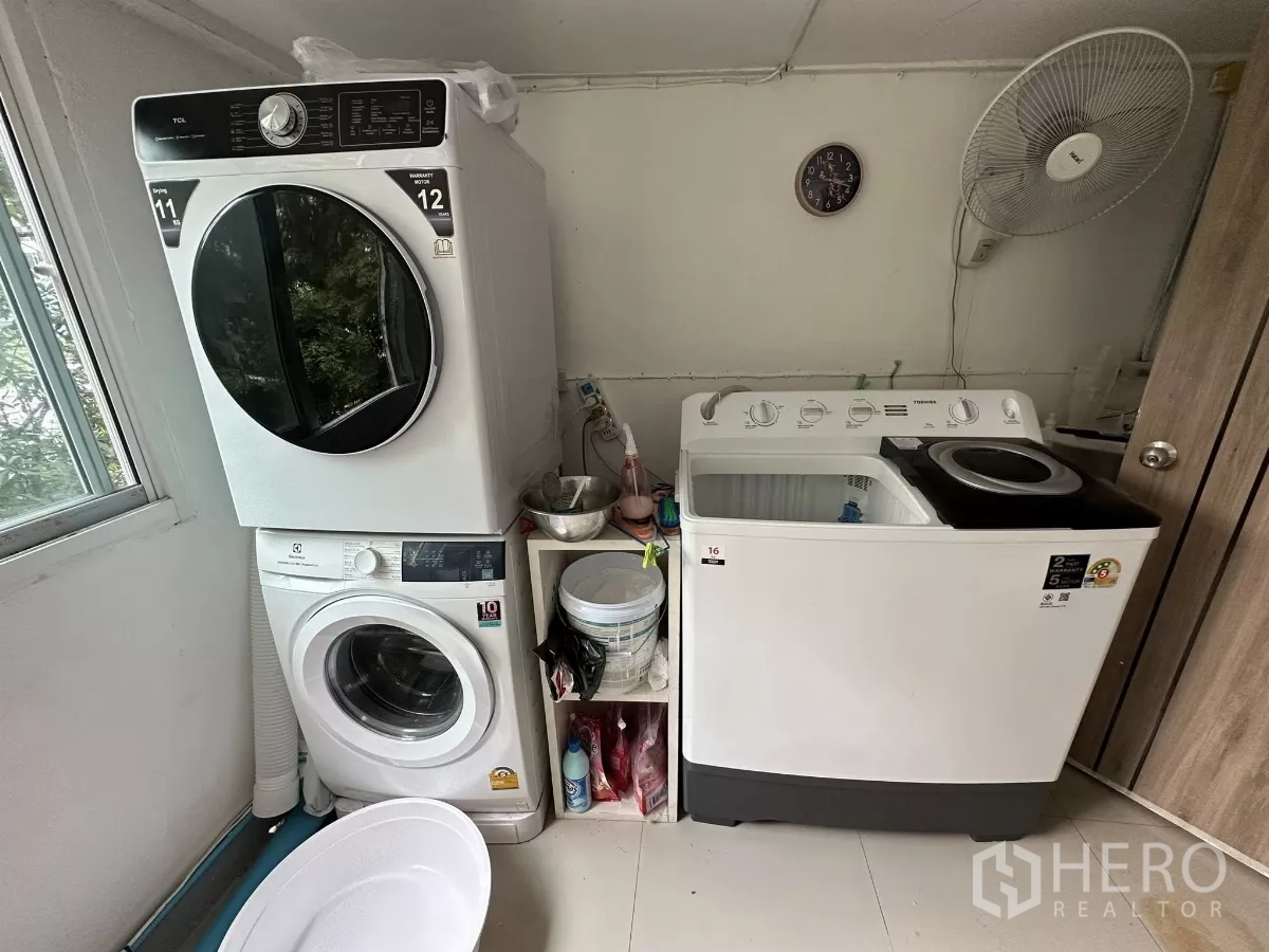 พื้นที่ขายปลีก ให้เช่า - มุมซักรีดเล็ก เครื่องซักอบแบบวางซ้อน และเครื่องซักผ้าเปิดฝา ข้างหน้าต่าง