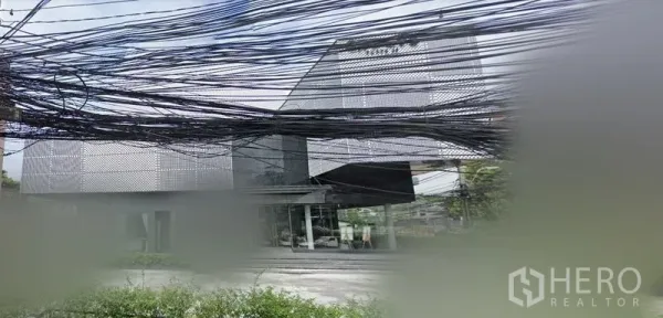 零售空间 出租在Huai Khwang, Bangkok - 曼谷辉煌区现代零售建筑外观，穿孔金属幕墙与整面玻璃店面，前方有可停车的空地，上方有电缆线。