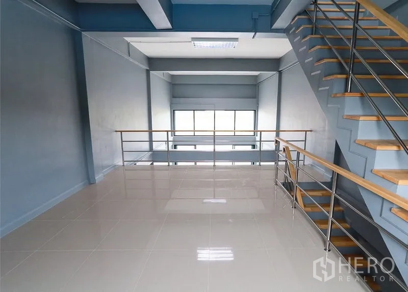 Shophouse for sale in Lam Luk Ka, Pathum Thani - Mezzanine workspace with railing and stairs overlooking large windows.