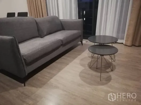 คอนโด ให้เช่าในWatthana, Bangkok - โซฟาผ้าสีเทาและโต๊ะกลางทรงกลมซ้อนกันสองตัวบนพื้นไม้ ข้างหน้าต่างระเบียง