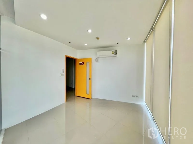 Office Space for rent in Khlong Toei, Bangkok - Corner office room with large windows, blinds, recessed lighting and a yellow-trimmed door.