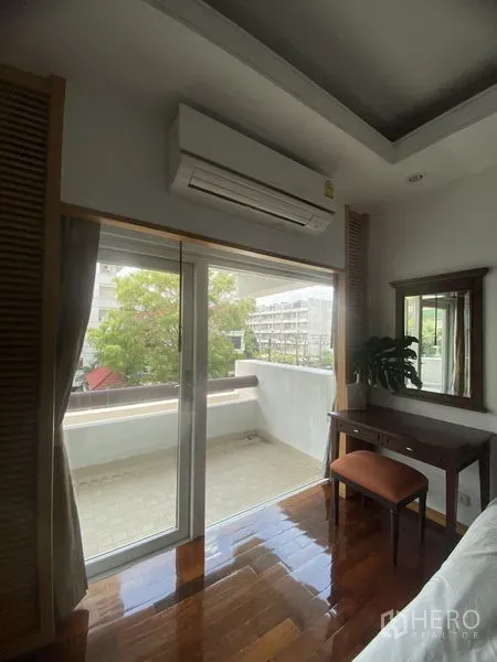 Condominium for rent - Bedroom corner with sliding glass doors to a spacious balcony, air conditioner, desk and hardwood floors overlooking greenery.