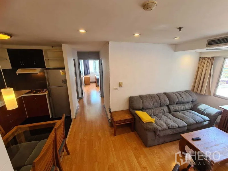 Condominium for rent in Ratchathewi, Bangkok - Open-plan living area with gray sofa connected to kitchen and dining.