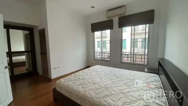 Townhouse for rent in Wang Thonglang, Bangkok - Sunlit bedroom with double bed, air conditioner, and two windows.