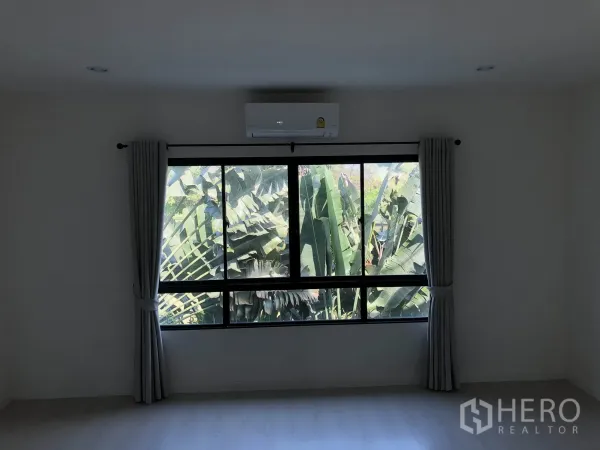 ทาวน์เฮาส์ ให้เช่าในBang Kapi, Bangkok - ห้องนอนสว่างพร้อมหน้าต่างบานใหญ่ ผ้าม่านสีเทาและเครื่องปรับอากาศ มองเห็นต้นไม้เขียวชอุ่ม