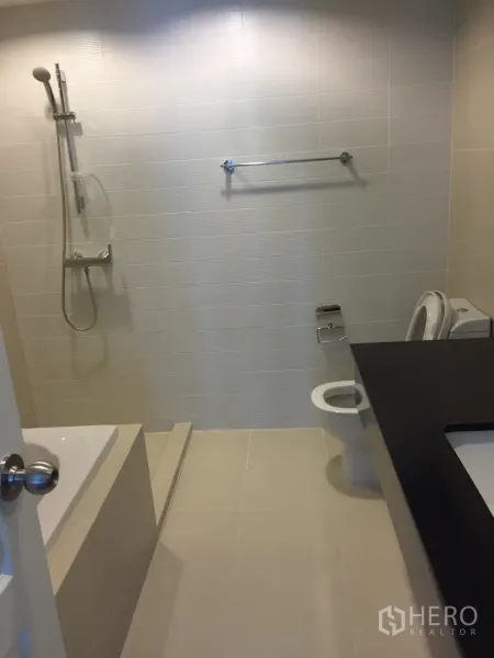 Condominium for rent in Huai Khwang, Bangkok - Contemporary bathroom with bathtub, handheld shower, toilet and long vanity counter.