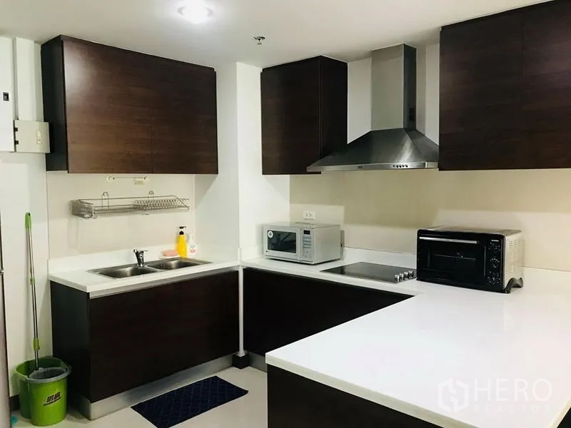 คอนโด ให้เช่าในPathum Wan, Bangkok - ครัวรูปตัวแอลตู้ไม้เข้ม เคาน์เตอร์สีขาว อ่างล้างจานคู่และเครื่องใช้ไฟฟ้า