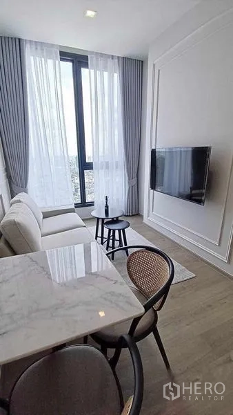 คอนโด ให้เช่า - ห้องนั่งเล่นติดทีวีแขวนผนังและหน้าต่างสูงมองเห็นวิวเมือง.