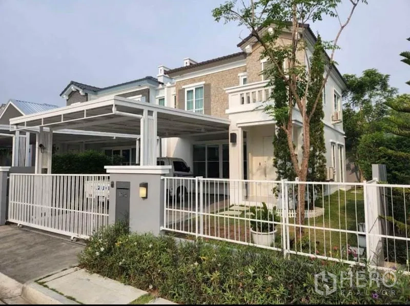 Detached House for rent in Prawet, Bangkok - Two-storey detached house with white fence, covered two-car carport, and landscaped front garden.