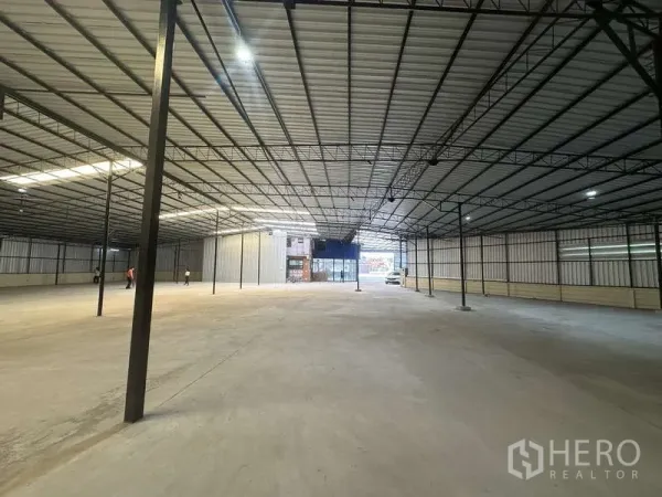 Warehouse for rent in Pak Kret, Nonthaburi - Deep warehouse hall with high ceiling, multiple support columns, and glass-front entry at the far end.