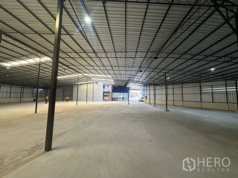 Warehouse for rent in Pak Kret, Nonthaburi - Deep warehouse hall with high ceiling, multiple support columns, and glass-front entry at the far end.