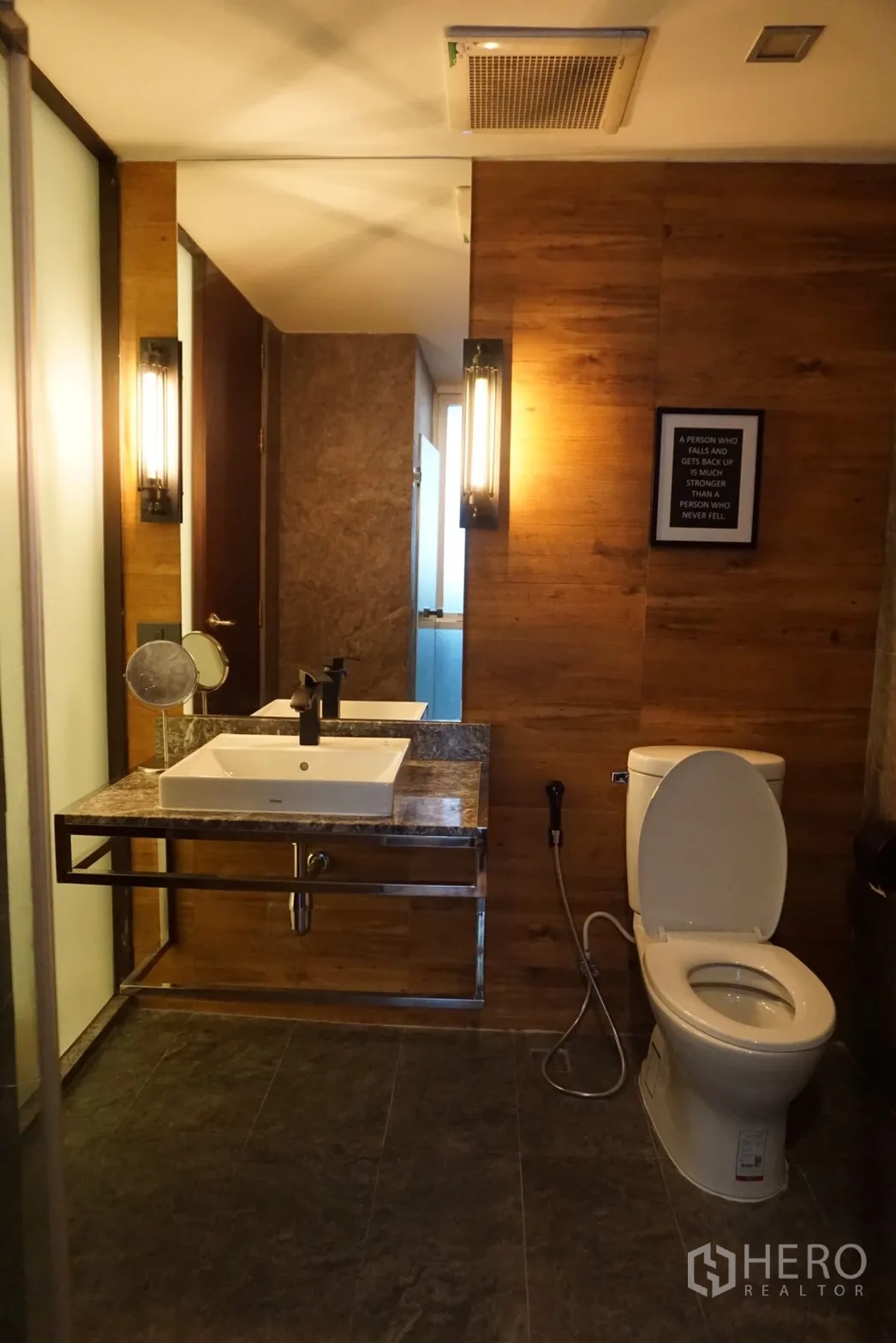 Condominium for rent or sale in Bang Rak, Bangkok - Contemporary bathroom with square vanity sink, marble counter, wall sconces and toilet in warm wood and stone finishes.