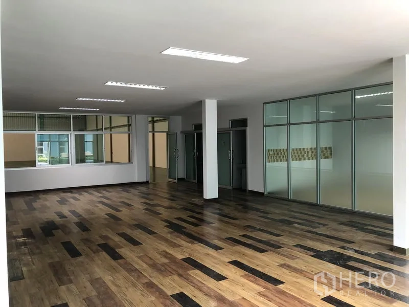 Factory for rent in Samut Prakan - Spacious office area with multiple glass rooms, ceiling lights and vinyl wood flooring.