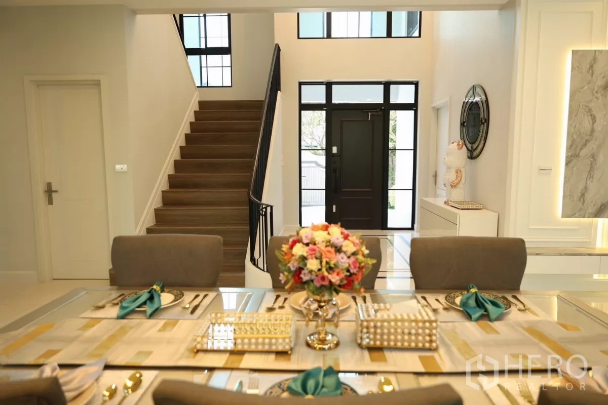 Detached House for rent or sale in Saphan Sung, Bangkok - Elegant dining table in foreground with staircase and double-height foyer behind.