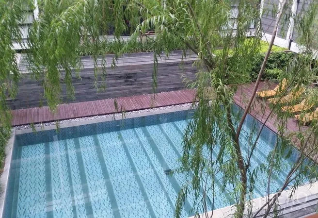 Condominium for rent or sale in Watthana, Bangkok - Outdoor swimming pool with timber deck surrounded by lush greenery in the condominium.