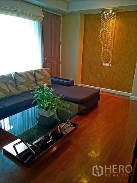 คอนโด ให้เช่าในPathum Wan, Bangkok - ห้องนั่งเล่นสบาย โซฟาเข้ามุม โต๊ะกลางกระจก ผนังลายไม้ และโคมไฟห้อย