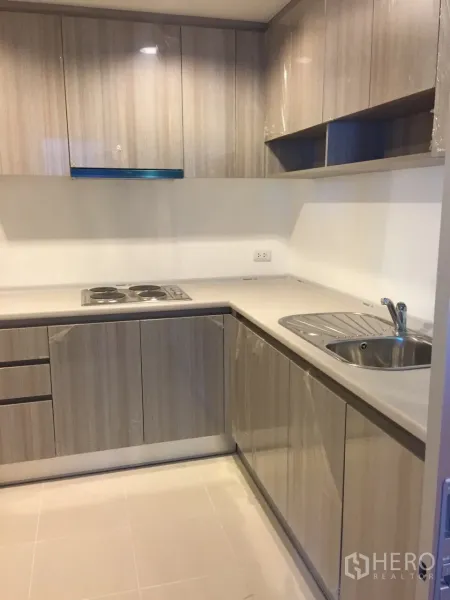 Condominium for rent in Huai Khwang, Bangkok - Modern U-shaped kitchen with built-in cabinets, electric cooktop and tiled flooring.