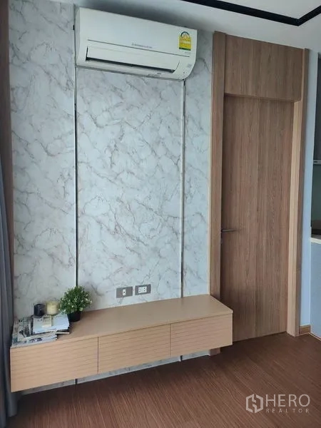 公寓 出租在Khlong Toei, Bangkok - 客厅内空调下方的电视柜与大理石纹装饰墙。