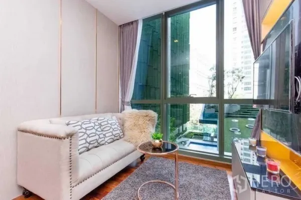Condominium for sale in Ratchathewi, Bangkok - Living room with floor-to-ceiling windows overlooking a landscaped courtyard and pool.