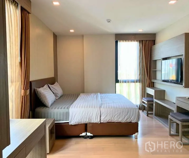 คอนโด ให้เช่า - ห้องนอนมาสเตอร์กว้างพร้อมเตียง ผนังทีวี โต๊ะทำงาน และหน้าต่างบานใหญ่