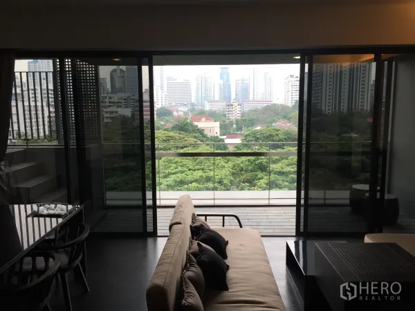 公寓 出租在Watthana, Bangkok - 客厅连接宽大阳台，可俯瞰绿意与曼谷天际线景观。