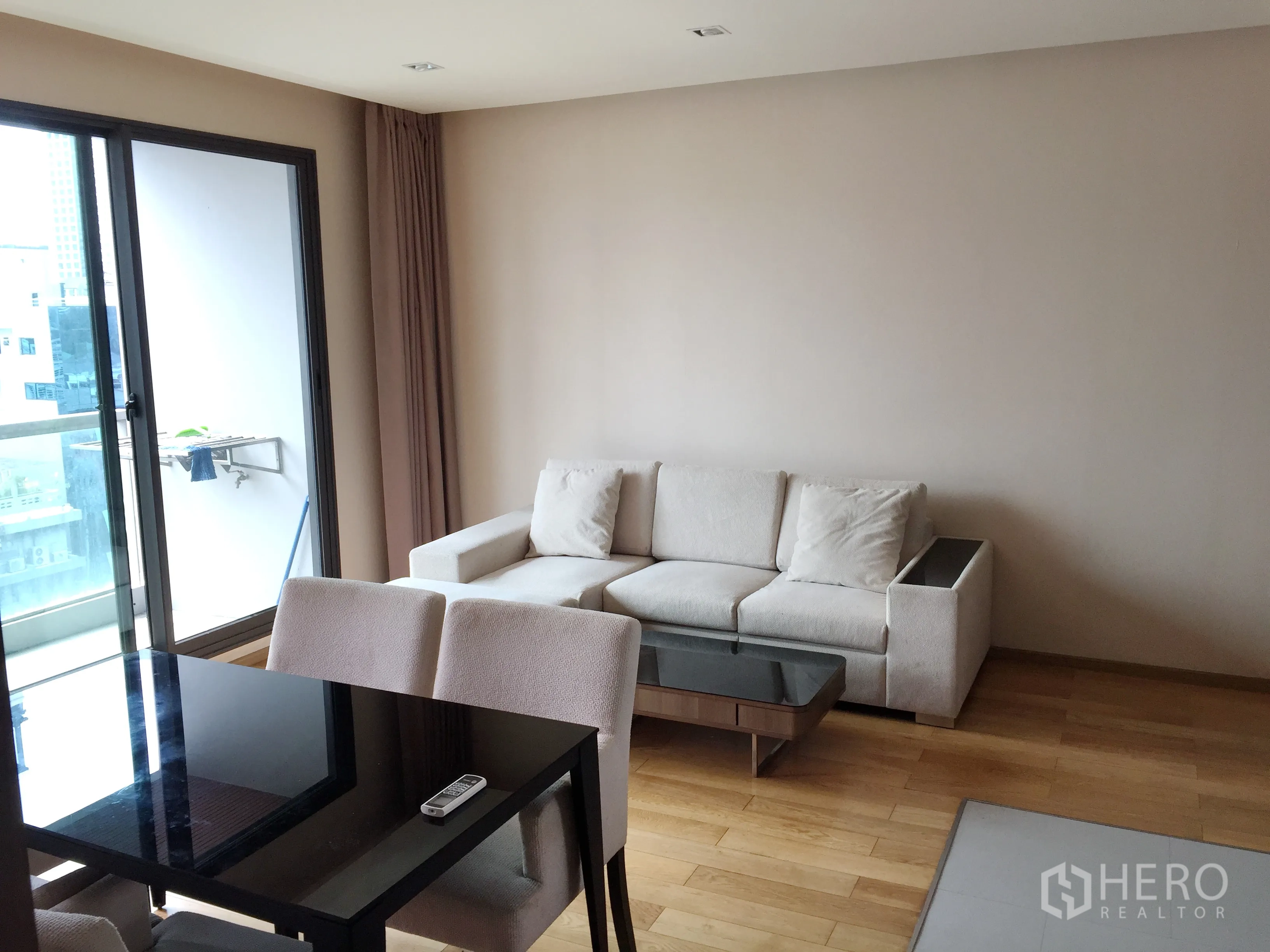 公寓 出租在Bang Rak, Bangkok - 采光充足的起居区，米色沙发与玻璃茶几，推拉门通往阳台。