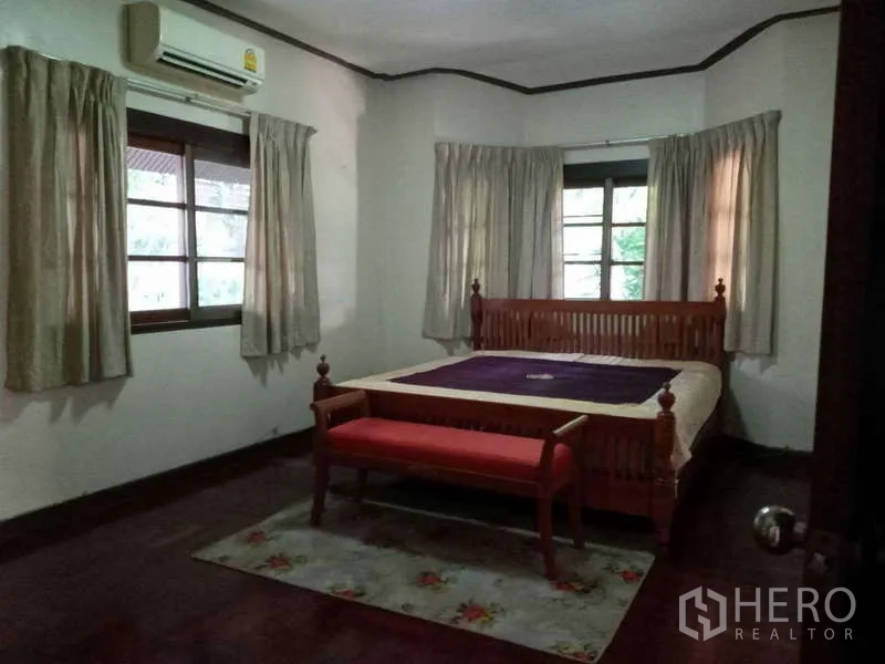 Detached House for rent in Khlong Toei, Bangkok - Air-conditioned bedroom with wooden bedframe and multiple windows.