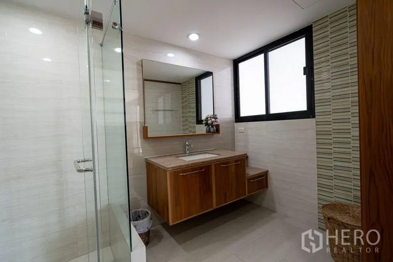 公寓 出售在Watthana, Bangkok - 明亮浴室，玻璃淋浴、窗户与带大镜子的木质洗手台。
