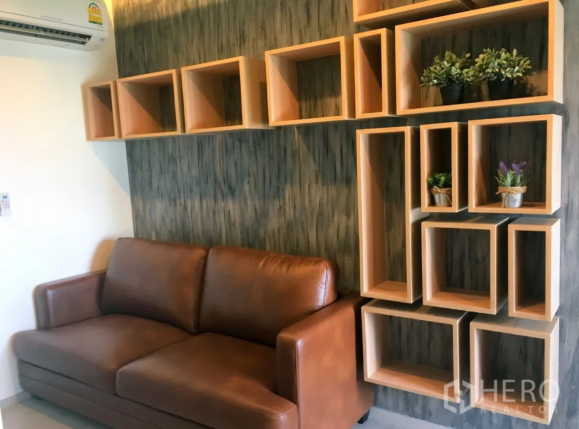 คอนโด ให้เช่าในKhlong Toei, Bangkok - ห้องนั่งเล่นโซฟาหนังสีน้ำตาล พร้อมชั้นวางดีไซน์เรขาคณิตและกระถางต้นไม้