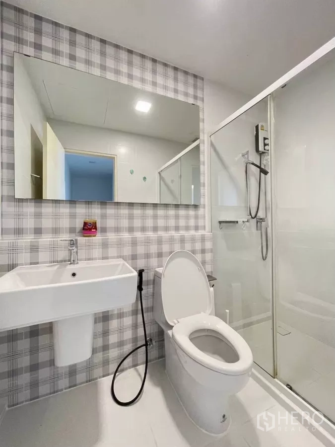 联排别墅 出租在Prawet, Bangkok - 浴室铺格纹瓷砖，大镜子、马桶与玻璃淋浴间。