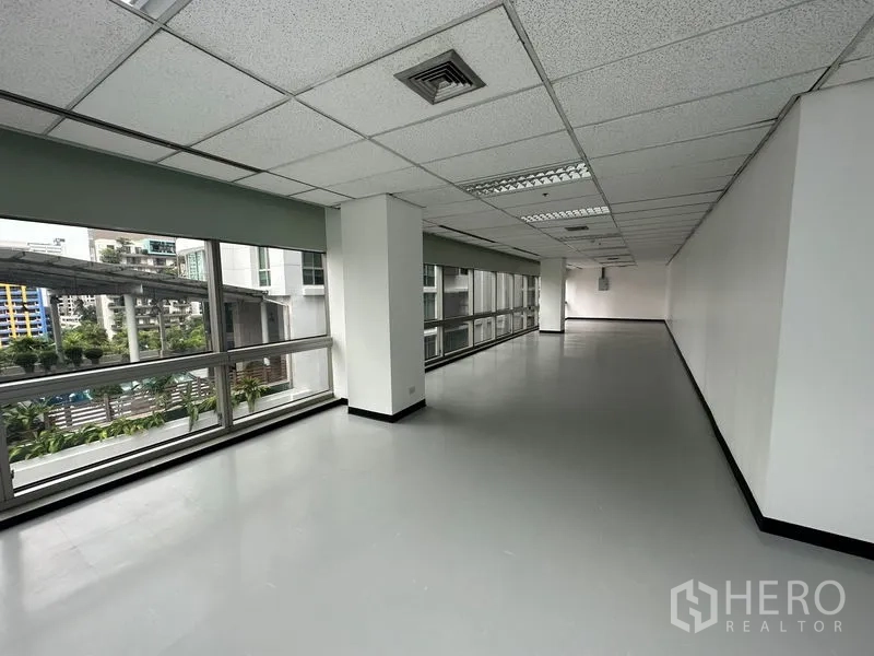 สำนักงาน ให้เช่า - โซนออฟฟิศยาวมีเสา พร้อมกระจกต่อเนื่อง มองเห็นต้นไม้และตึกสูง.