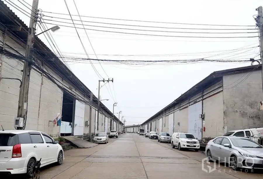 Warehouse for rent in Bang Phli, Samut Prakan - Industrial estate roadway with parallel warehouse rows and ample parking on both sides.