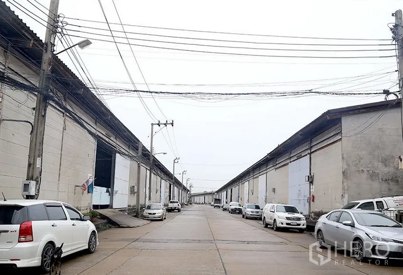 Warehouse for rent in Bang Phli, Samut Prakan - Industrial estate roadway with parallel warehouse rows and ample parking on both sides.