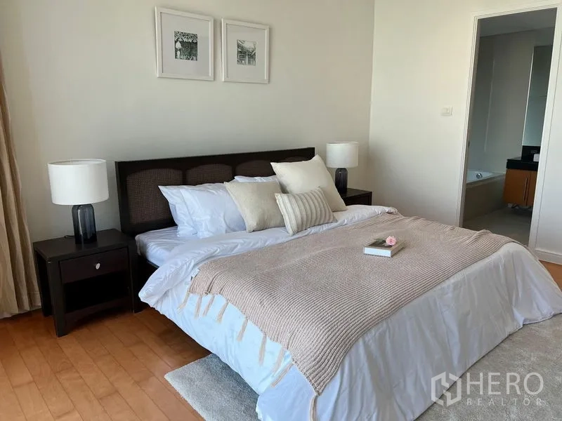 Condominium for rent in Watthana, Bangkok - Primary bedroom with soft neutral bedding and doorway to the ensuite bathroom with tub.