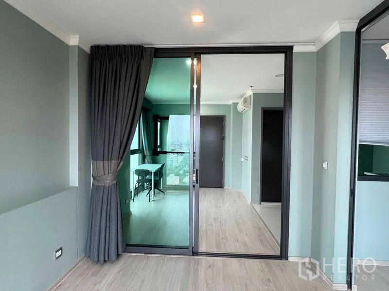 Condominium for sale in Ratchathewi, Bangkok - Glass sliding door separating bedroom and living area with blackout curtains and wood flooring.