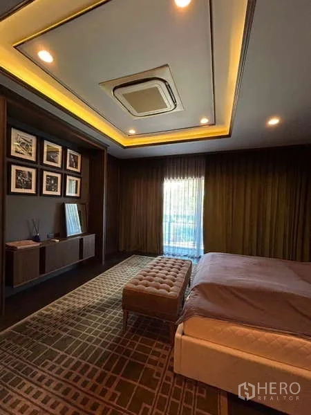 独立式住宅 出租在Bang Kapi, Bangkok - 宽敞主卧，托盘式天花灯光，双人床与长凳，落地窗帘与内置搁架。