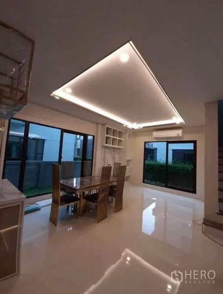 Detached House for rent or sale in Prawet, Bangkok - Dining area with glass-top table, LED cove lighting and full-height windows to the garden.