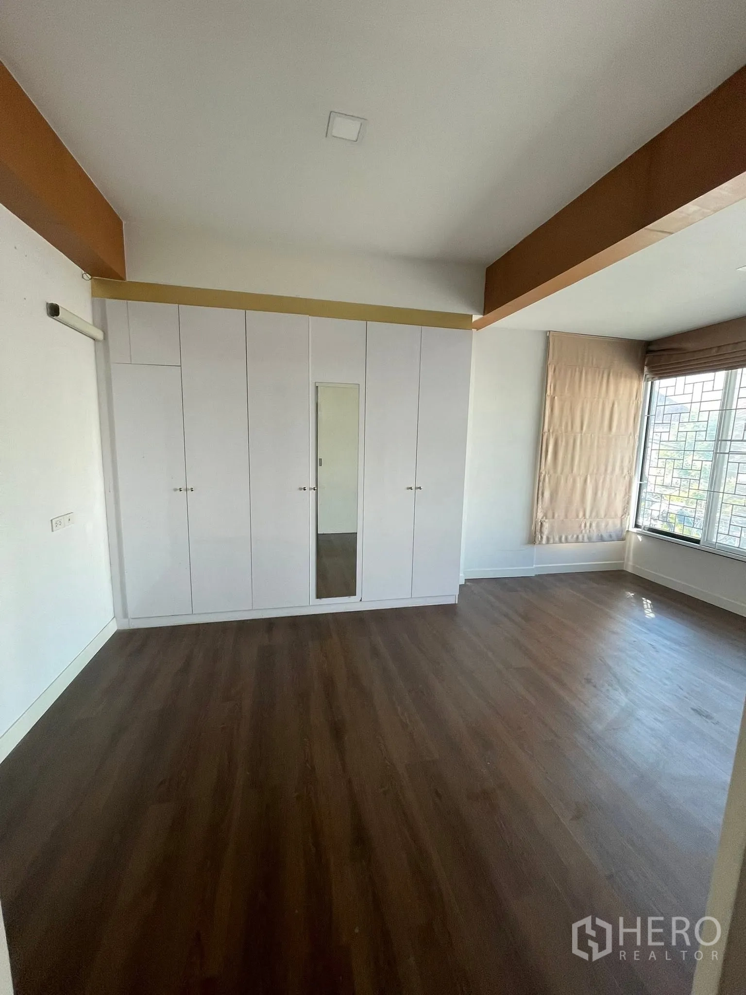 Detached House for rent or sale in Lam Luk Ka, Pathum Thani - Spacious bedroom with white built-in wardrobes, wood floors, and a large window with blinds.