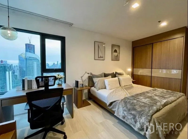 Condominium for rent in Pathum Wan, Bangkok - Spacious master bedroom with sliding wardrobe, bed, and study desk by a panoramic window.