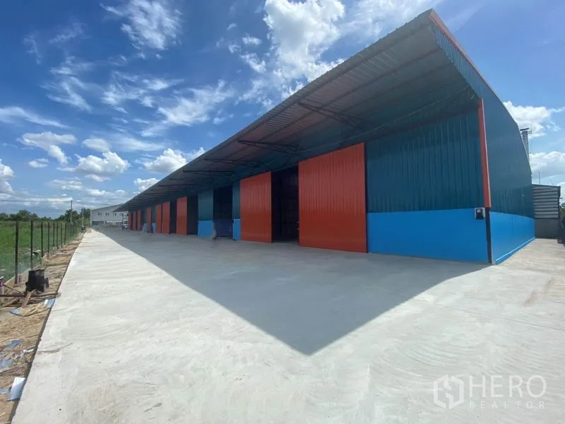 工厂 出租在Khlong Luang, Pathum Thani - 广角外景，整排工厂红门与开阔混凝土场地，晴空背景。