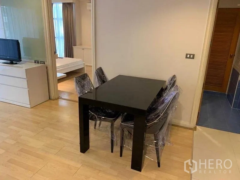 คอนโด ให้เช่าในPathum Wan, Bangkok - พื้นที่นั่งเล่นและรับประทานอาหาร โต๊ะสีดำ ตู้วางทีวี พื้นไม้โทนอ่อน และประตูบานเลื่อนสู่ห้องนอน