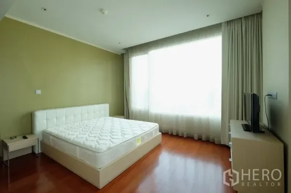 Condominium for rent in Bang Rak, Bangkok - Bright bedroom with large window, white upholstered bed and warm wood flooring.