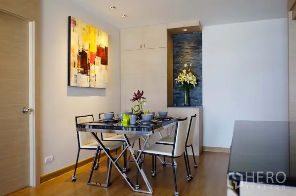 Condominium for rent or sale in Si Racha, Chon Buri - Modern dining area with glass-top table for four, wall art and built-in cabinetry on warm wooden floors.