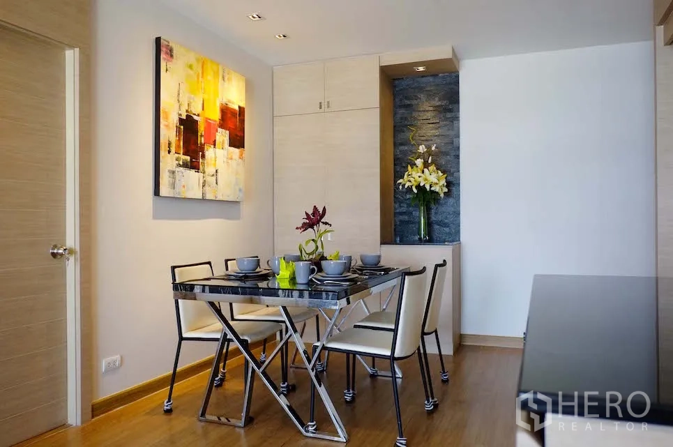 Condominium for rent or sale in Si Racha, Chon Buri - Modern dining area with glass-top table for four, wall art and built-in cabinetry on warm wooden floors.