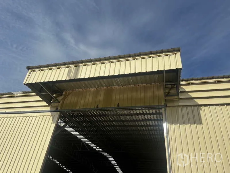 Warehouse for rent or sale in Pak Kret, Nonthaburi - Close-up of warehouse entrance canopy and tall metal rolling door under corrugated cladding.