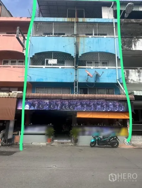 อาคารพาณิชย์ ให้เช่าหรือขายในBang Lamung, Chon Buri - มุมมองด้านหน้าของอาคารพาณิชย์สีฟ้า 3 ชั้น ชั้นล่างเป็นหน้าร้าน มีกันสาดและรถจักรยานยนต์จอดริมถนน