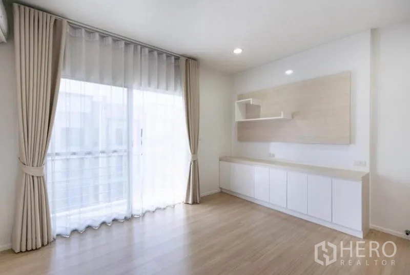 Townhouse for rent or sale in Watthana, Bangkok - Bright room with sliding glass doors, beige drapes and sleek storage cabinet.